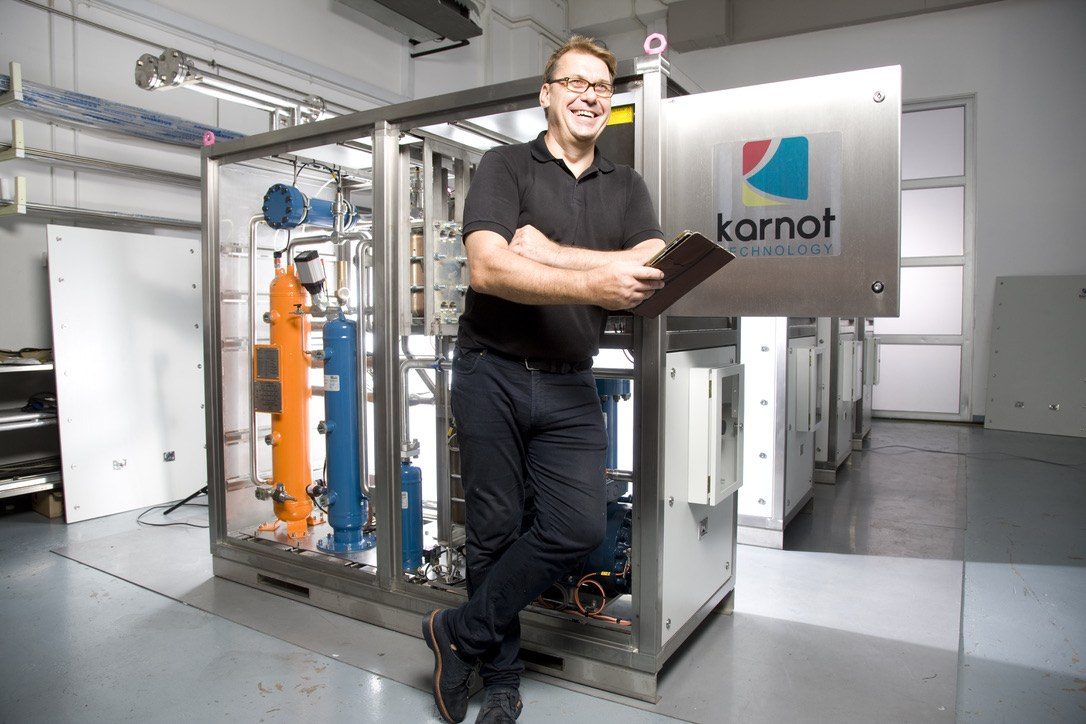 Stuart Cox, founder of Karnot, standing beside a stainless-steel heat pump skid he designed and built