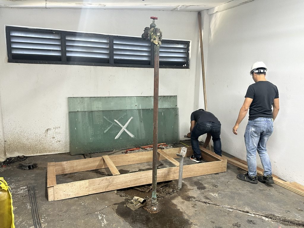 Two workers building timber formwork for a concrete plinth in a plant room before a heat pump is installed
