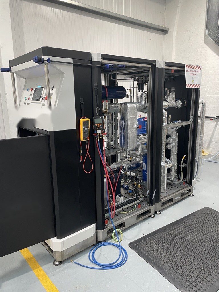 Ultra-low-temperature cooling unit on a test bay with gauges connected and a system-under-pressure sign